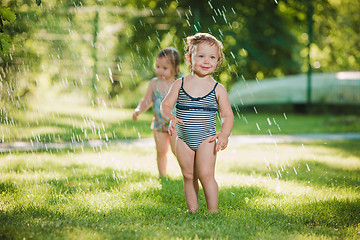 Image showing The two little baby girls playing with garden sprinkler.