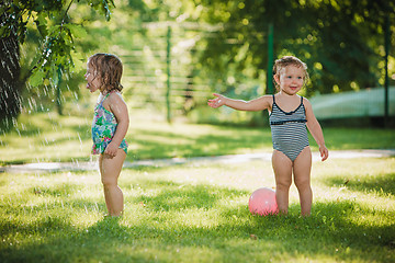 Image showing The two little baby girls playing with garden sprinkler.