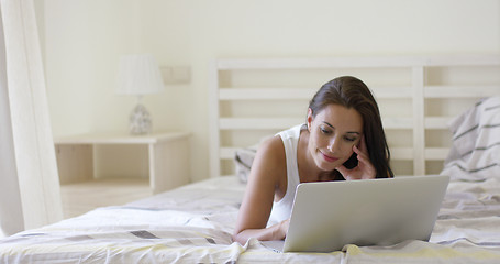 Image showing Young woman laying down in bed using laptop