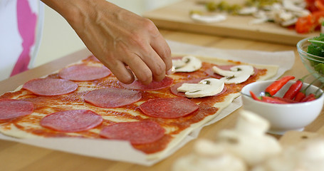 Image showing Woman making a homemade salami and mushroom pizza