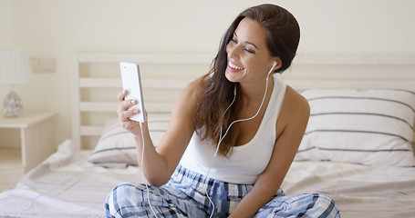 Image showing Giggling woman using device with ear buds in bed