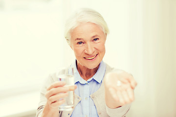 Image showing happy senior woman with water and medicine at home