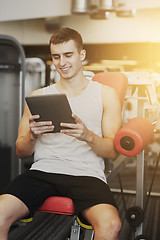 Image showing smiling young man with tablet pc computer in gym