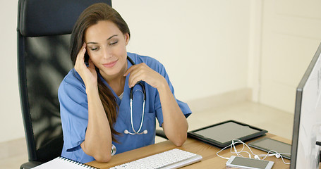 Image showing healthcare worker wearing scrubs sits at computer