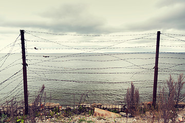 Image showing barb wire fence over gray sky and sea