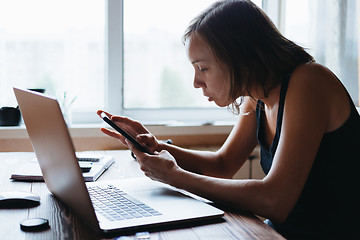 Image showing Woman working on computer and looking at the phone