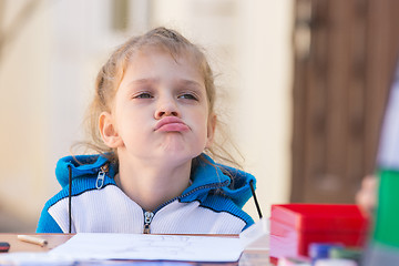 Image showing Frustrated girl sitting at a table in the courtyard of the house and looking cocky