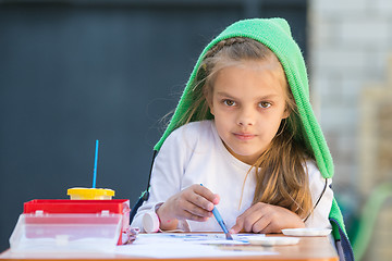 Image showing Pleased girl draws paints at the table and looked at the frame