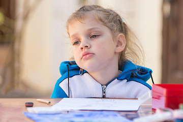 Image showing Frustrated girl sitting at a table in the yard and sad looks nowhere