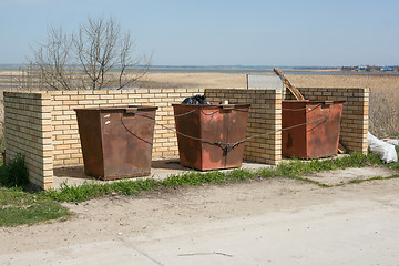Image showing Three garbage tank linked metal cable are at the designated place and enclosed by brick