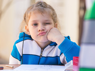 Image showing Sad girl thought doing drawing at a table in the yard