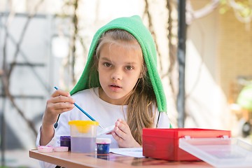 Image showing Girl draws paints in the yard in the spring sunny day and looked into the frame