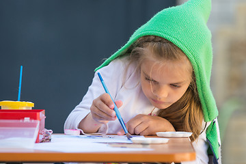 Image showing Girl enthusiastically paints watercolors sitting at a table in the yard