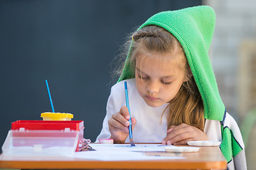 Image showing Slightly disheveled girl watercolor paints sitting at the table in the yard