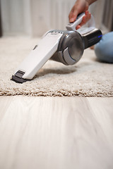 Image showing Female hand holding cordless vacuum cleaner and cleaning beige carpet