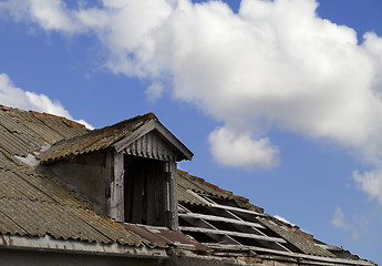 Image showing Old tile roof with holes and blue sky with clouds