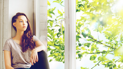 Image showing sad pretty teenage girl sitting on windowsill