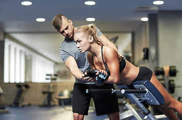 Image showing woman with personal trainer flexing muscles in gym