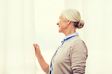 Image showing happy senior woman looking through window at home