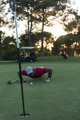 Image showing golf player blowing ball in hole with sunset in background