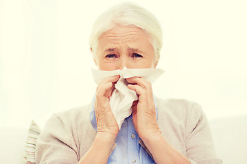 Image showing sick senior woman blowing nose to paper napkin