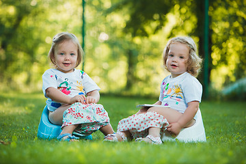 Image showing The two little baby girls sitting on pottys against green grass