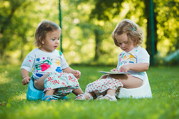 Image showing The two little baby girls sitting on pottys against green grass