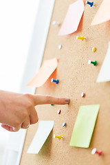 Image showing hand pointing to cork board with stickers and pins