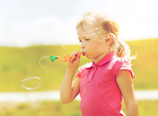 Image showing little girl blowing soap bubbles outdoors