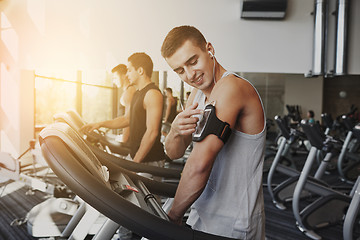 Image showing man with smartphone exercising on treadmill in gym