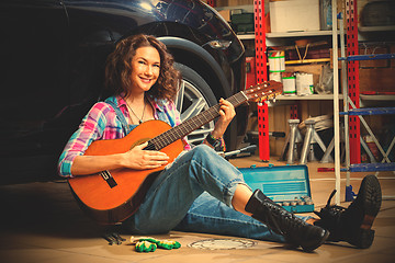 Image showing woman mechanic in overalls sitting near the wheels of the car an