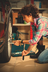 Image showing woman mechanic in overalls tighten the fixing bolts on the wheel