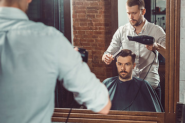 Image showing Young handsome barber making haircut of attractive man in barbershop