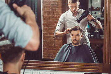 Image showing Young handsome barber making haircut of attractive man in barbershop