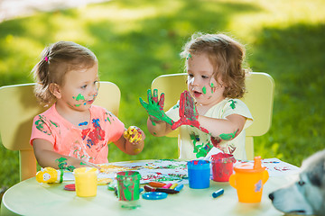 Image showing Two-year old girls painting with poster paintings together against green lawn