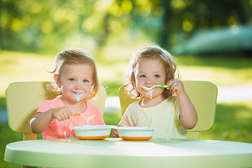 Image showing Two little girls sitting at a table and eating together against green lawn