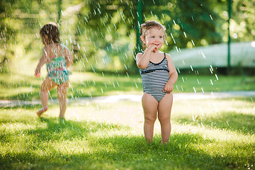 Image showing The two little baby girls playing with garden sprinkler.