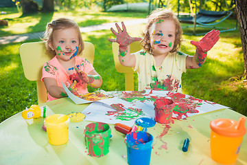 Image showing Two-year old girls painting with poster paintings together against green lawn