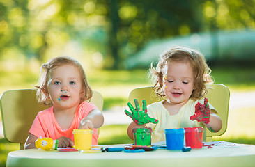 Image showing Two-year old girls painting with poster paintings together against green lawn