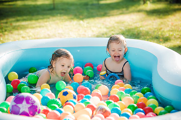 Image showing The two little baby girls playing with toys in inflatable pool in the summer sunny day