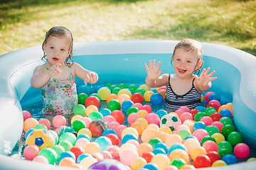 Image showing The two little baby girls playing with toys in inflatable pool in the summer sunny day