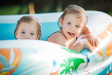 Image showing The two little baby girls playing with toys in inflatable pool in the summer sunny day