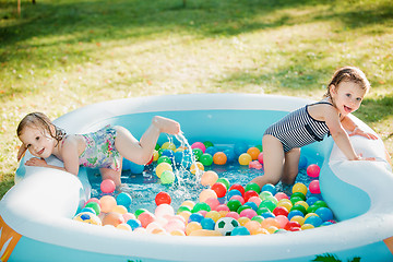 Image showing The two little baby girls playing with toys in inflatable pool in the summer sunny day