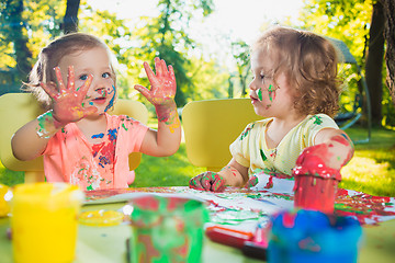 Image showing Two-year old girls painting with poster paintings together against green lawn