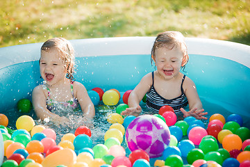 Image showing The two little baby girls playing with toys in inflatable pool in the summer sunny day