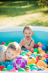 Image showing The two little baby girls playing with toys in inflatable pool in the summer sunny day