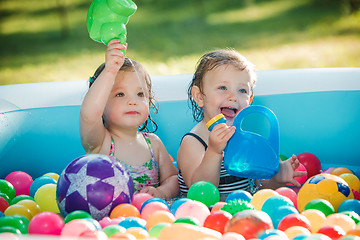 Image showing The two little baby girls playing with toys in inflatable pool in the summer sunny day