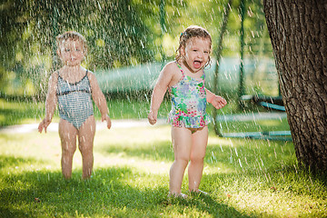 Image showing The two little baby girls playing with garden sprinkler.