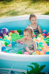 Image showing The two little baby girls playing with toys in inflatable pool in the summer sunny day