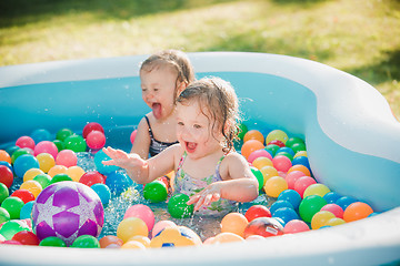 Image showing The two little baby girls playing with toys in inflatable pool in the summer sunny day